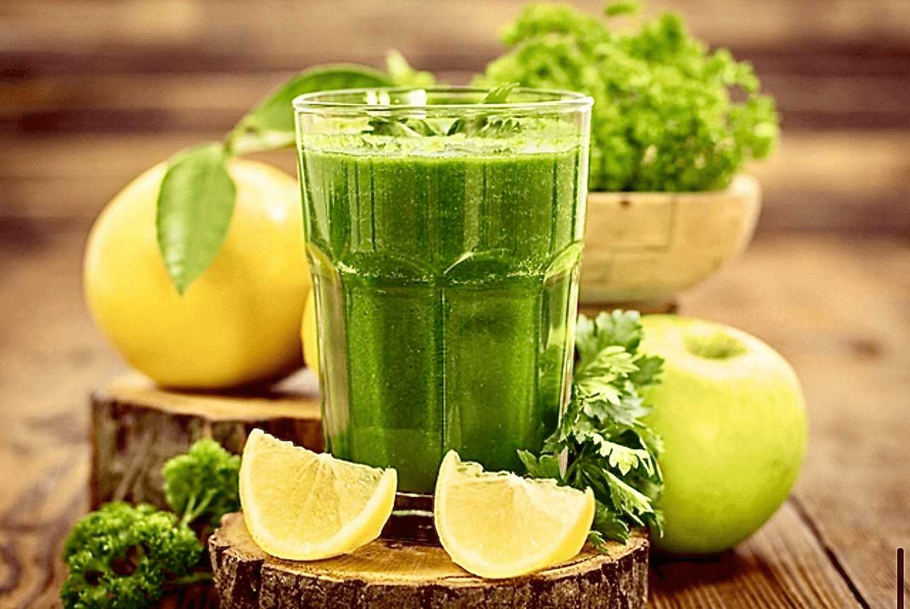 A glass of green juice with lemons and apples.