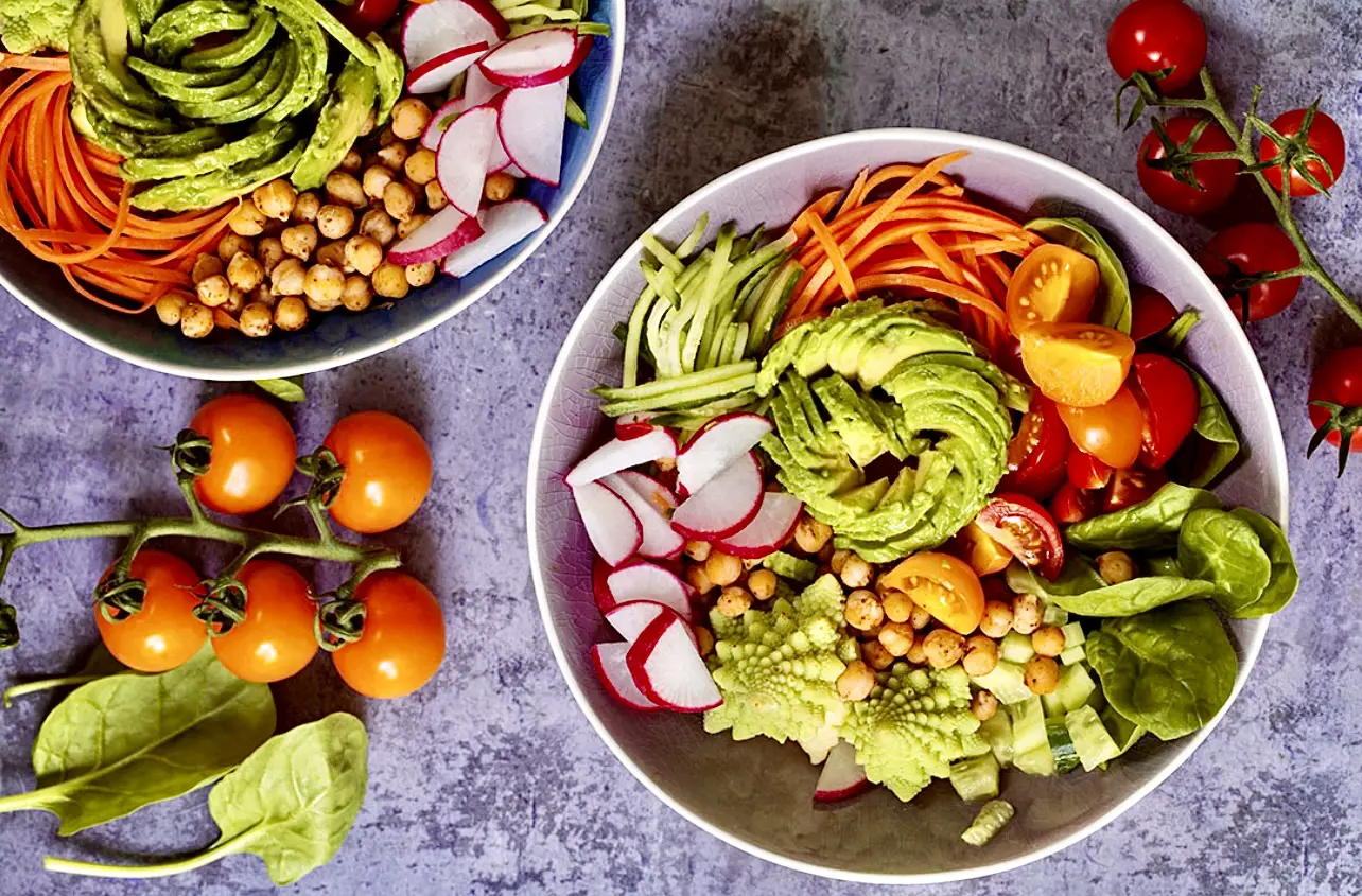 Two bowls of food on a table with vegetables.